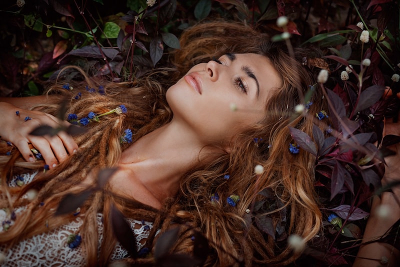 hippy woman lying on the ground covered with flowers and leaves in her hair